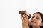 Woman holding piece of wood against wall