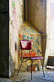 A Red Chair Sits Beside A Weathered Wall With Painted Graffiti; Barcelona, Spain