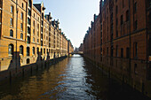 Braune Backsteingebäude entlang eines Kanals unter blauem Himmel; Hamburg, Deutschland