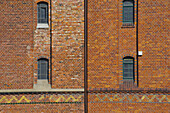 Fassade eines Backsteingebäudes mit Fenstern und einem gemusterten Streifen; Hamburg, Deutschland.
