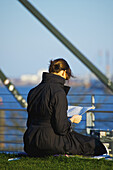 Eine Frau sitzt lesend am Ufer des Wassers; Hamburg, Deutschland
