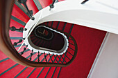 Eine rote Treppe mit braunem Geländer und schwarzen Metallstäben an einer weißen Wand; Hamburg, Deutschland