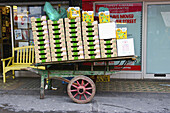 Ein verwitterter Holzwagen vor einem mit Kisten gefüllten Schaufenster in Soho; London, England