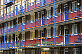 Backsteingebäude mit blauen Geländern und Türen auf den Balkonen und einem rot gestrichenen Streifen auf der unteren Hälfte der Mauern; London, England.