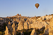 Bunter Heißluftballon fliegt über die raue Landschaft; Kappodokien, Türkei