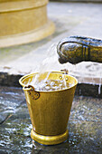 Wasser, das aus einem Wasserhahn in einen kleinen gelben Eimer fließt; Ulpotha, Embogama, Sri Lanka