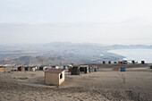 Small Shed Scattered On A Sandy Landscape With Haze And A View Of A Lake; Ancon, Peru
