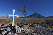 Kreuze an einem Straßenrand und der Vulkan Licancabur in der Ferne; Chile