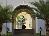 Treppe, die zu einem gewölbten Eingang mit Laternenpfählen und Palmen führt