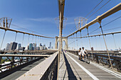 Paar auf einem Tandemfahrrad auf dem Fußgängerweg an der Brooklyn Bridge, New York City, New York, Vereinigte Staaten