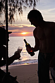 Gemeinsame Nutzung einer Flasche Wein am Strand bei Sonnenuntergang; Sihanoukville, Kambodscha