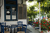 Traditional Wooden Chairs And Red Geraniums Outside A Taverna; Apollonia, Sifnos, Cyclades, Greek Islands, Greece