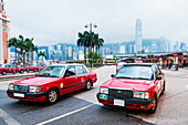 Einige rote Taxis in Kowloon mit der Skyline von Hongkong Island als Hintergrund; Kowloon, Hongkong, China