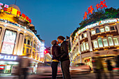 Ein Paar, das sich küsst, mit dem Verkehr und den Fußgängern im Hintergrund; Hongkong, China