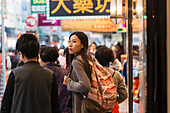 Eine junge Frau mit Rucksack unter vielen Fußgängern auf den belebten Straßen von Kowloon; Hongkong, China