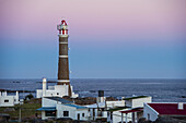 Leuchtturm und Häuser in der Abenddämmerung entlang der Küste; Cabo Polonio, Uruguay