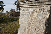 Beschriftete römische Säule mit dem kapitolinischen Tempel in der Ferne; Thuburbo Majus, Tunesien.