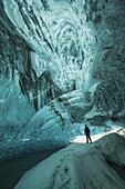 Person, die unter der Vatnajorkull-Eiskappe in einer großen Eishöhle steht; Island