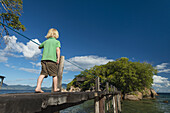 Junger Junge geht entlang einer schmalen Holzbrücke zu einer Mini-Insel vor Mumbo Island, Malawi-See; Malawi