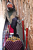 Gondoliere bindet seine Gondel an einen Pfosten neben einem Gebäude an einem Kanal; Venedig, Italien