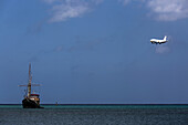 Kommerzielles Passagierflugzeug im Anflug auf den internationalen Flughafen von Aruba, überfliegt das blaue Meer und Fischtrawler, Surfside Beach; Aruba
