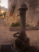 Cast iron public water fountain with the head of a lion at dusk; Grottazzolina, Marche region, Italy