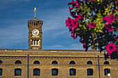 Clock tower and building with blossoming flowering blurred in the foreground, in St Katharine Docks Marina, London, UK; London, England