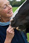 Close up of smiling mature woman pinching a horse nose