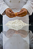 Close up of a chef hands holding an egg above a heap of flour over a glass table