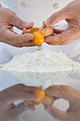 Close up of a chef hands breaking an egg above a heap of flour over a glass table