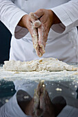 Close up of a chef rubbing his hands over a dough on a glass table