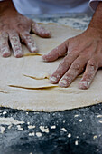 Nahaufnahme eines Kochs mit mehlverschmierten Händen beim Kneten eines Pizzateigs