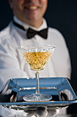 Nahaufnahme eines lächelnden Kellners mit weißen Handschuhen, der ein Getränk auf einem Silbertablett anbietet