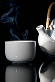 Nahaufnahme einer dampfenden Teetasse mit grünem Tee und Detail einer Teekanne mit Holzgriff