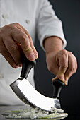 Close up of a chef hands chopping an onion with a double blade mezzaluna knife