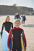 Junge und Mädchen mit Surfbrettern an einem Strand, gefolgt von Menschen