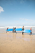 Männer und Kinder, die mit Surfbrettern an einem Strand spazieren gehen