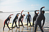 Rückenansicht eines Surflehrers und einer Gruppe von Schülern, die sich an einem Strand dehnen