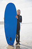 Lächelndes Mädchen, das ein Surfbrett aufrecht hält