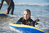 Lächelndes und nasses Mädchen im Meer, das sich an ihrem Surfbrett festhält