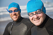 Two men wearing bathing caps and goggles smiling