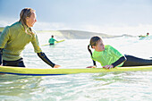 Frau im Meer hält ein Surfbrett, auf dem ein Mädchen liegt