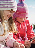 Zwei junge Mädchen tragen Wollmützen und halten einen mp3-Player