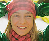 Lächelndes junges Mädchen mit einer Wollmütze und den Händen auf dem Kopf