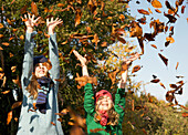 Zwei lächelnde Mädchen, die Blätter in die Luft werfen