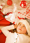 Girl lying under a red and white Christmas tree looking up