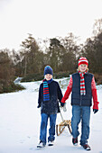 Porträt von zwei Jungen, die im Schnee spazieren gehen und einen Schlitten ziehen
