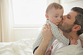 Vater küsst kleinen Jungen im Schlafzimmer