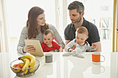 Couple Sitting at Table with Baby Twins Using Digital Tablet