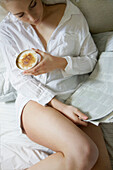 Frau trinkt Cappuccino im Bett und liest Zeitung